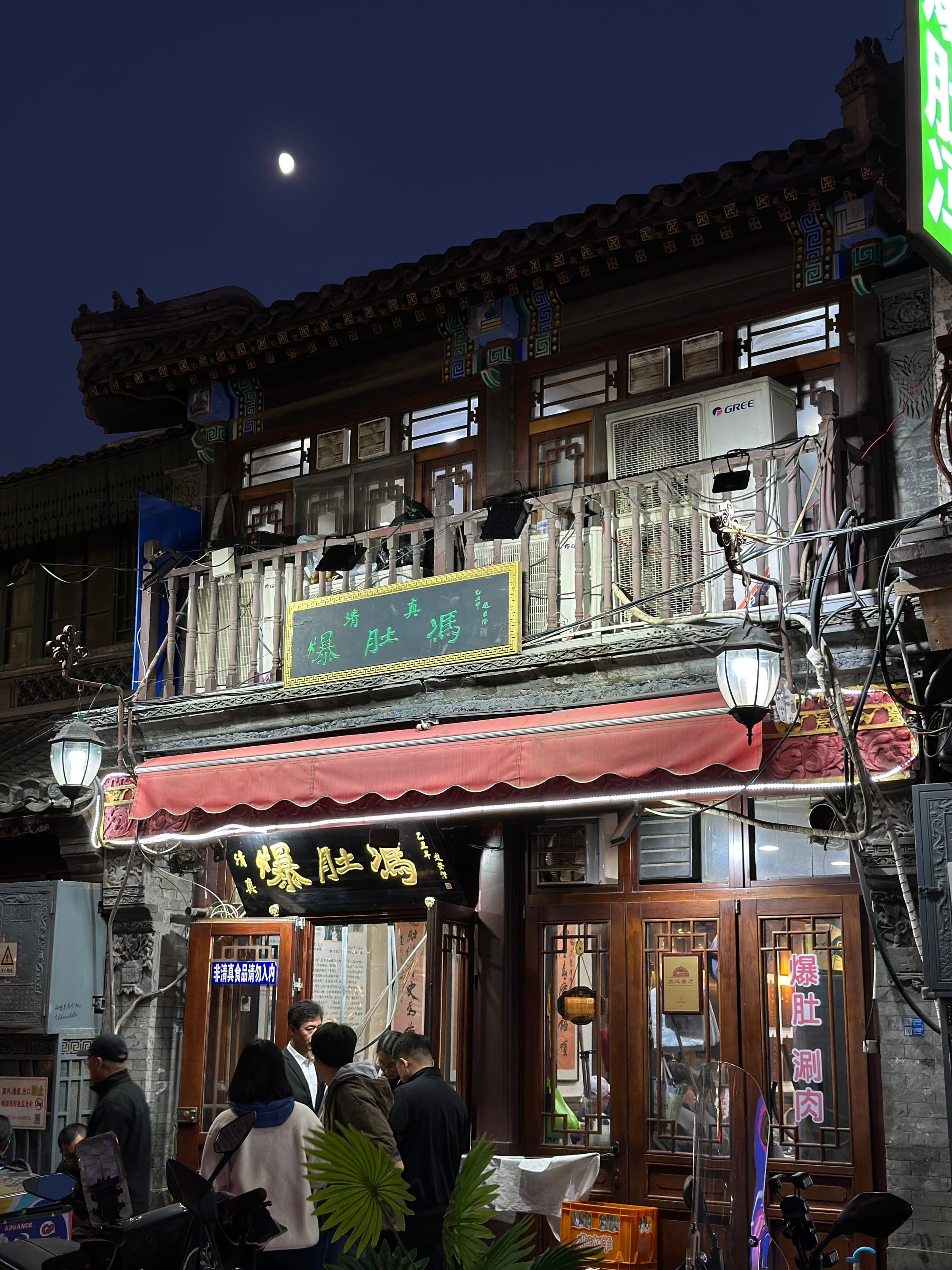 Façade d'un petit restaurant traditionnel de Qianmen le soir à Pékin, enseignes lumineuses et clients attablés