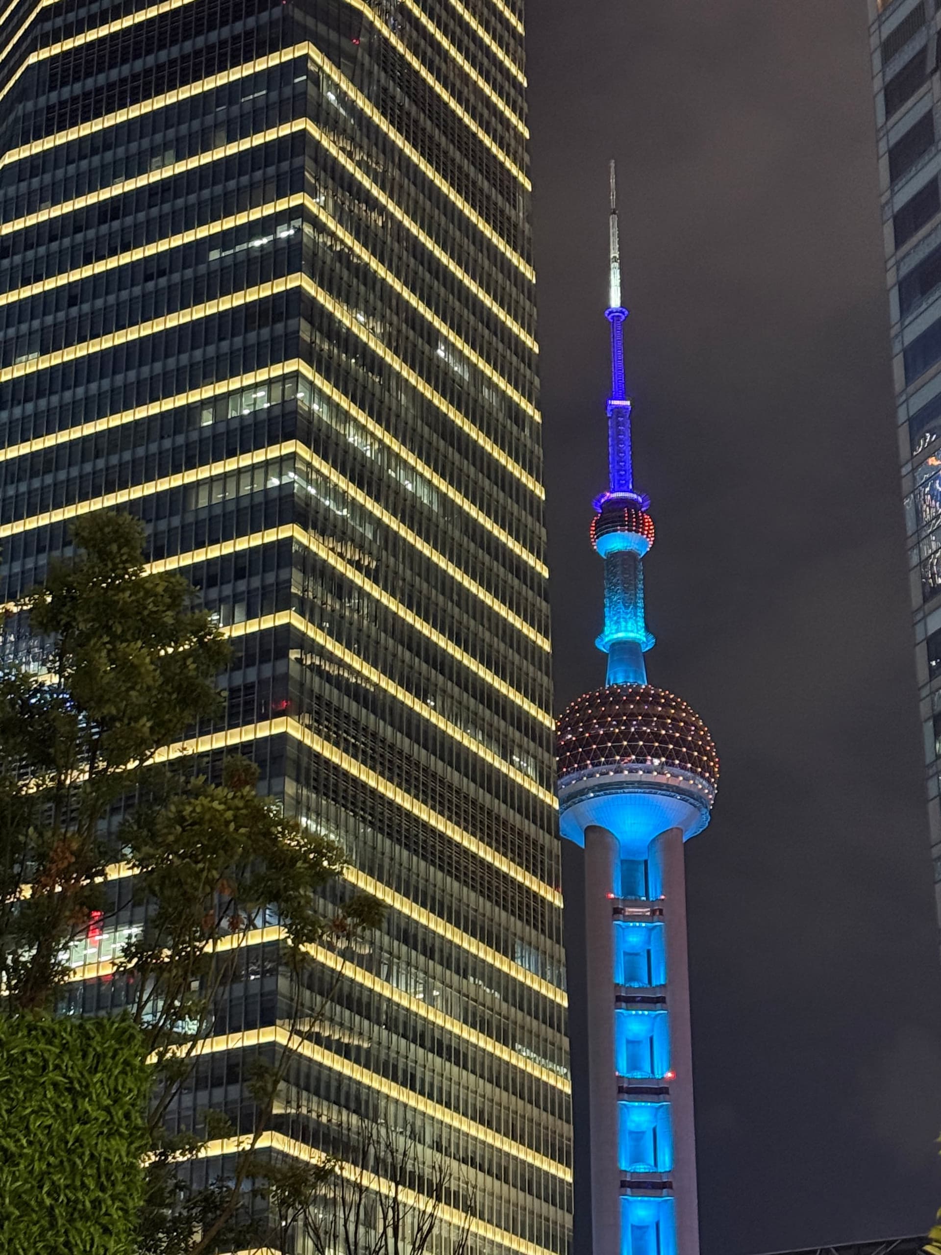 Perle de l'Orient illuminée en bleu et rouge la nuit à Shanghai, cadrage rapproché depuis le Bund, gratte-ciel doré du World Financial Center à gauche