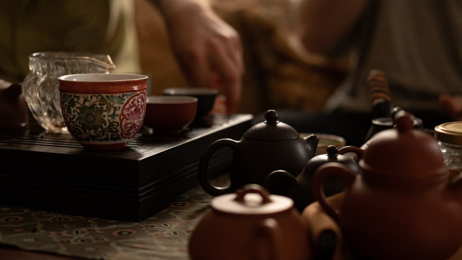 Table de dégustation de thé chinois, plateau noir à rainures portant une tasse en porcelaine décorée, pichet en verre et théières en terre brune au premier plan